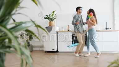 丈夫和妻子在厨房跳舞，拿着拖把和掸子做家务